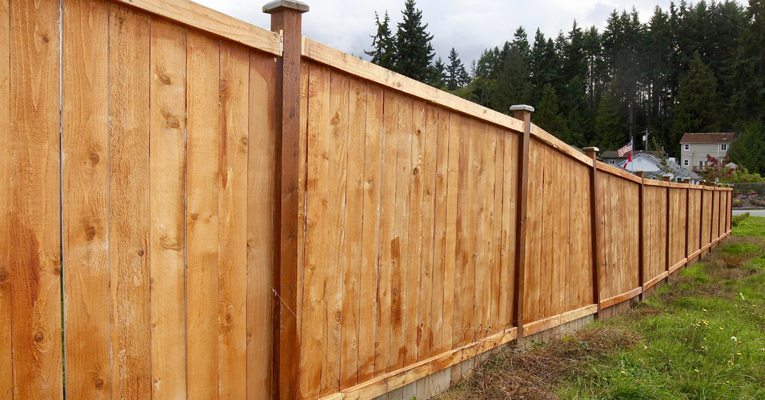Wooden fence on uneven ground with trees and houses in the background