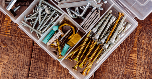 Assorted screws in a plastic container on a wooden surface