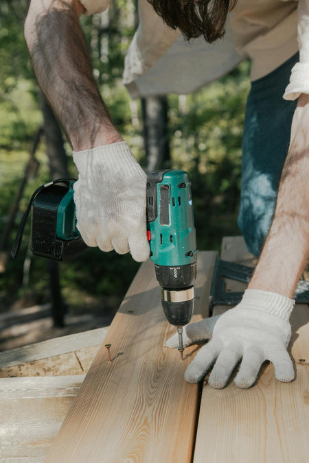 Person using a cordless drill on wooden planks outdoors