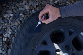 Person applying glue to a glue tread sidewall patch on a tire with a gravel background