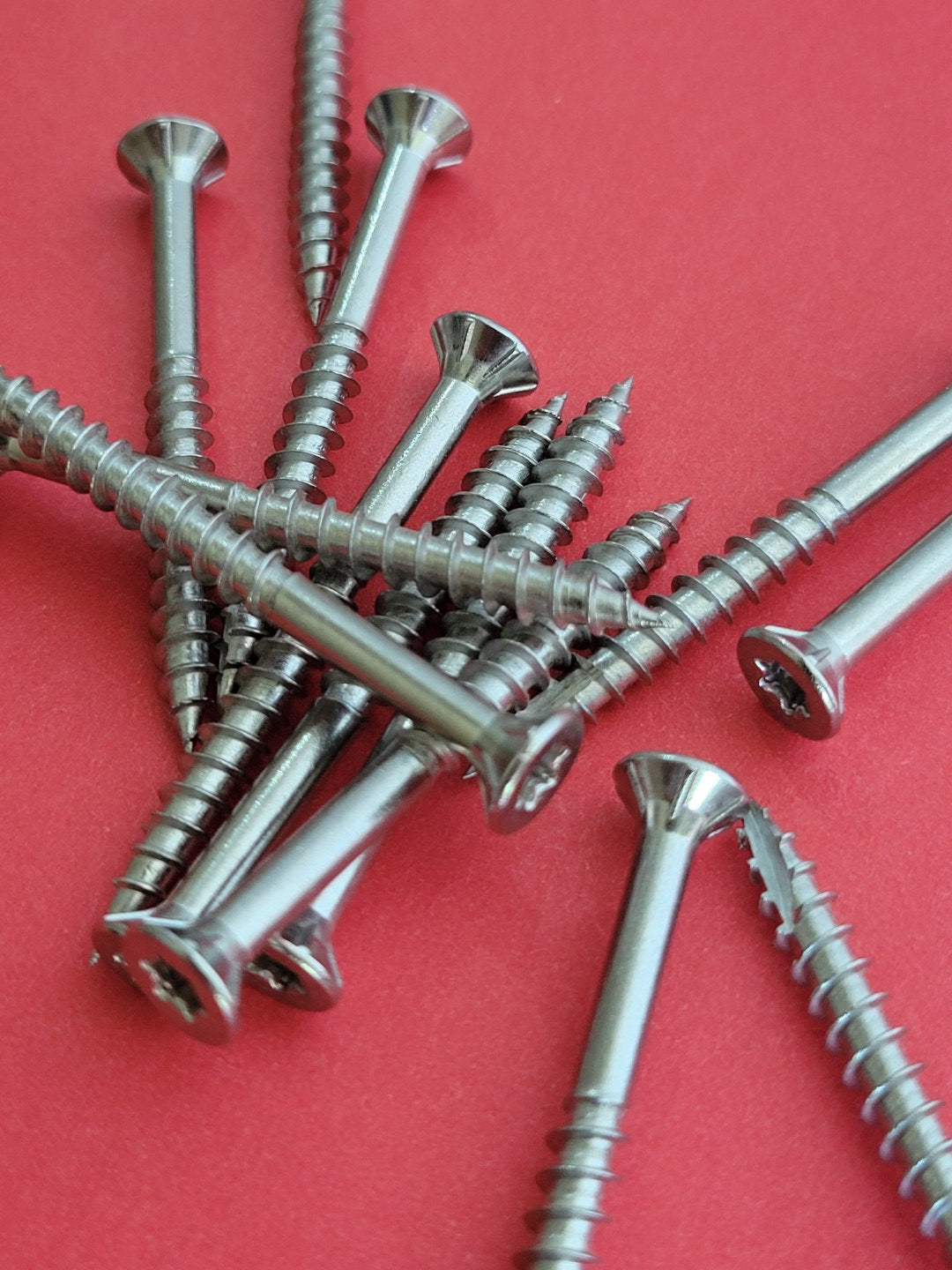 Pile of stainless steel all purpose wood screws on red background