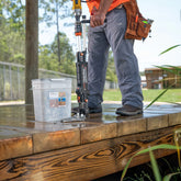 Person using a timber drive on a wooden surface with tools and a bucket in the background.