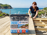 Person working on a wooden structure with a container of Eagle Claw screws in the foreground, set against a scenic ocean backdrop.