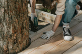 Person working on a wooden deck with a tree in the background
