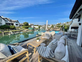 Outdoor seating area with striped cushions by a pool and waterfront view.