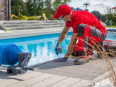 Person in red shirt and hat working on a pool deck with tools