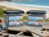 Two containers of exterior wood screws on a wooden table with tools and a beach in the background