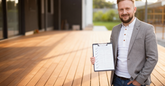 Man holding a clipboard with a document on a wooden deck